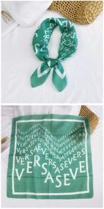 Detail of emerald green square scarf with white geometric letters and silk texture