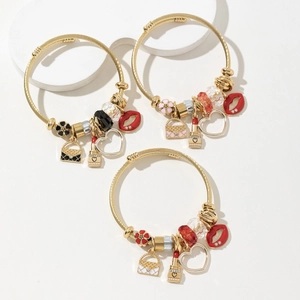 Adjustable gold twisted bangles with lipstick and heart charms on white pedestals