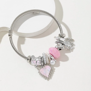 Silver twisted cable bracelet with pink heart and carriage charms on a white surface