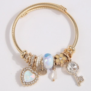 Gold-tone twisted bangle bracelet with heart and key charms and pearls on white background