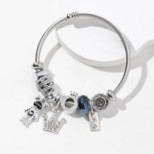 Bracelet à perles argenté avec breloques couronne et ours sur un socle blanc minimal