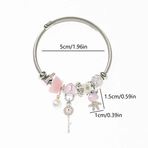 Détail du bracelet en maille d'acier avec breloques cœur rose, ours et clé