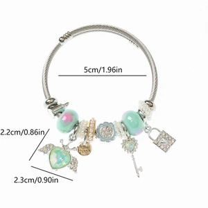 Dettaglio del bracciale in acciaio con ciondoli a forma di ali di cuore, chiave e lucchetto