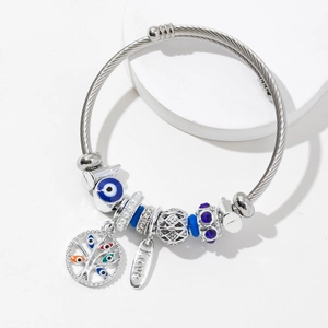 Silver steel cable bracelet with Tree of Life and Evil Eye charms on white pedestal