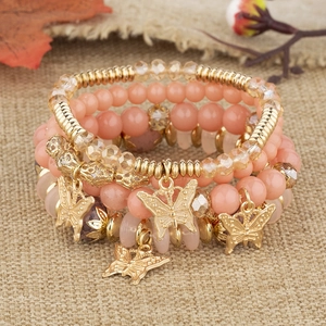 Détail de bracelets bohèmes superposables avec perles roses et breloques papillons dorés