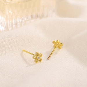 Exquisite hollow gold flower stud earrings with a central crystal on textured fabric
