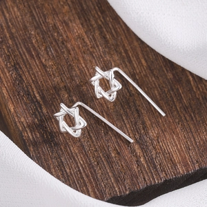 Macro shot of S925 silver hexagram earrings on textured wood and white fabric