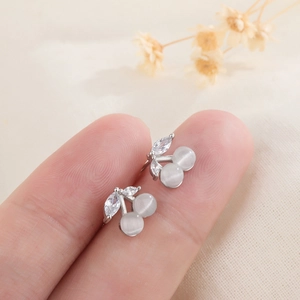 S925 silver cherry stud earrings with white cat-eye stones and zircon leaves held by hand