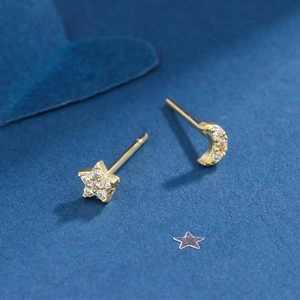 Asymmetric gold star and moon stud earrings with sparkling cubic zirconia on blue background