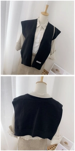 Detail of a black knitted vest with a V-neckline and white decorative tag on the hemline