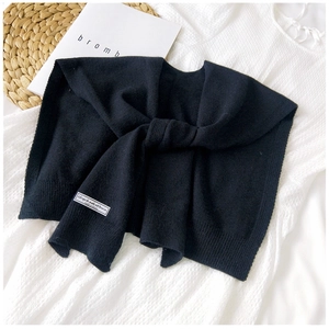 Detail of black knitted shawl with woven label on a white shirt in a lifestyle setting