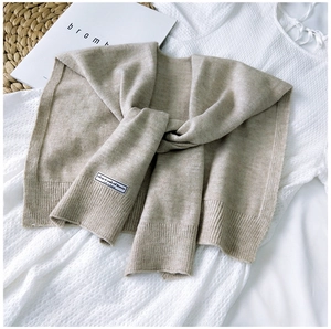 Detail of soft beige knitted shawl with ribbed edges and decorative fabric label on fabric