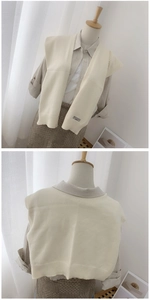 Detail of cream knit vest with ribbed hem and decorative black tag on front and back