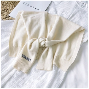 Close-up of cream knitted shawl wrap with woven label on a white textured dress