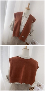 Detail of burnt orange knit shawl vest featuring ribbed texture and small logo patch