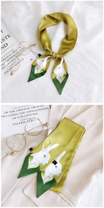 Detail of green silk twilly scarf with cute rabbit print styled on a beige blazer