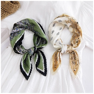 Detail of pleated paisley square scarves tied in bows on a white lace background