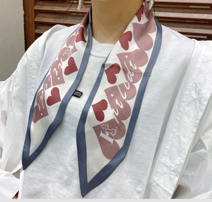 Detailed view of long narrow white scarf with pink heart patterns and artistic text print