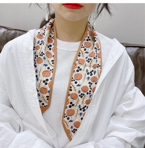 Detail of floral and pumpkin print narrow silk scarf tied on neck with brown edge