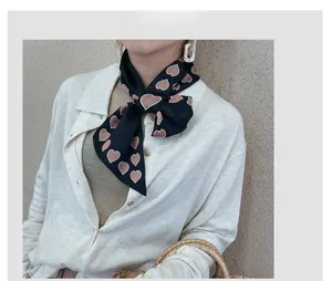Close-up of black silk scarf with brown heart patterns styled on a knitted cardigan