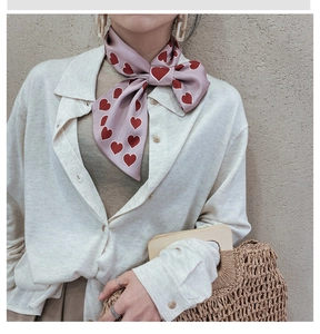 Detail of a pink silk scarf with red heart prints tied in a bow on a woman's neck