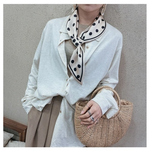 Detail of a minimalist polka dot scarf styled with a white shirt and straw handbag