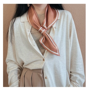 Detail of elegant caramel silk scarf with white H logo and border on beige knitwear