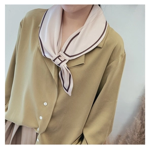 Detail of elegant silk scarf with H-letter print and dark coffee border on mustard shirt