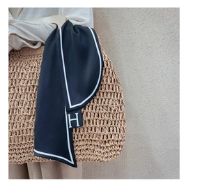 Detail of navy silk scarf with H-letter logo tied to a straw bag for elegant styling