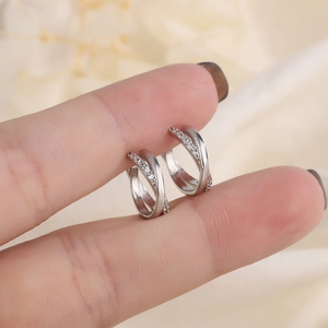 Elegant silver crossover hoop earrings with zircon stones held by a person