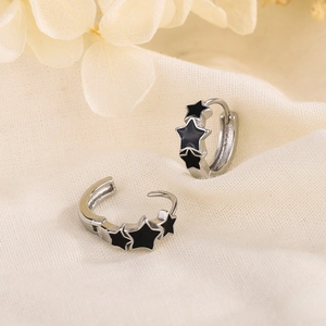 Silver hoop earrings featuring three black enamel stars on textured linen background