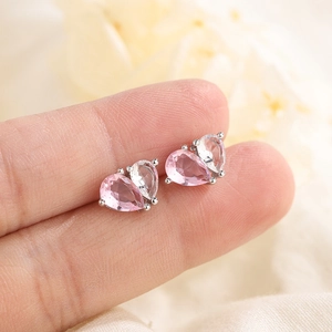 Elegante Herz-Ohrstecker mit rosa und klaren Birnenschliff-Steinen auf einem Finger