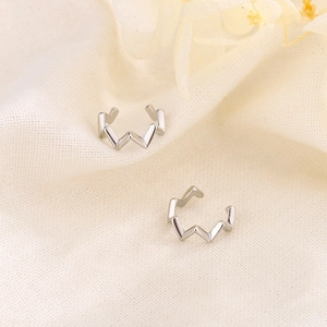 Minimalist silver wave ear cuff with polished zigzag design on soft beige fabric