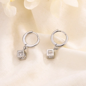Silver hoop earrings with hollow cube charm and sparkling zircon on beige linen