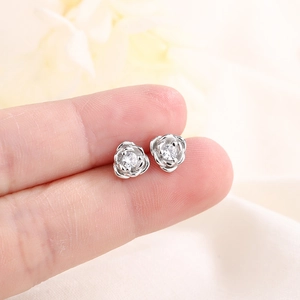 Detailed silver rose stud earrings with zircon stone center shown for size scale
