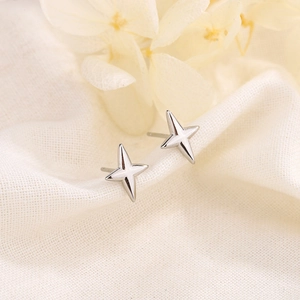 Minimalist silver four-pointed star stud earrings on elegant textured fabric