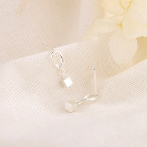 Minimalist silver wave studs with geometric cube pendants on textured linen fabric