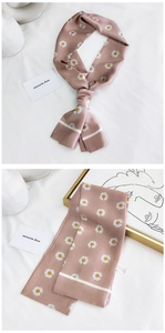 Gros plan d'une écharpe étroite rose à motif de marguerites sur un tissu blanc texturé