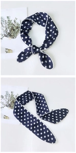 Navy blue polka dot silk scarf tied in a bow and laid flat on a white surface