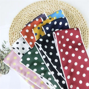 Polka dot silk scarf collection in multiple colors on a straw mat with green leaves
