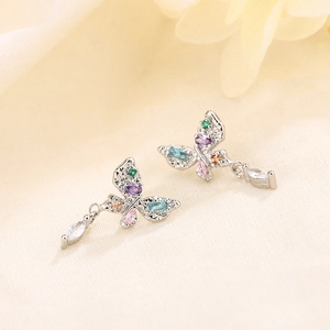 Elegant butterfly earrings with colorful zircons and drop pendants on cream fabric