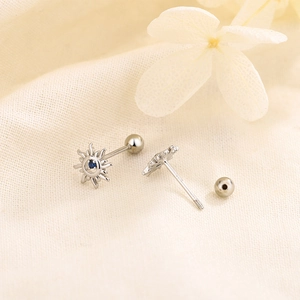 Silver sun stud earring with blue zircon and screw ball back on beige fabric