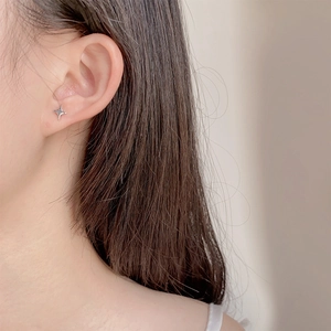 Minimalist asymmetric silver star studs worn on ear for a modern and sleek aesthetic look