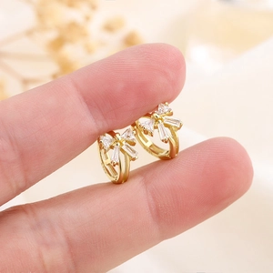 Boucles d'oreilles créoles nœud doré avec zircons sertis tenues par les doigts