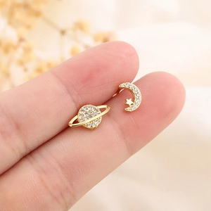 Asymmetric gold moon and planet stud earrings with white zircon stones held by fingers