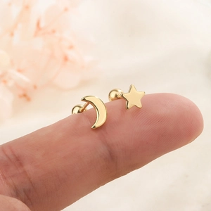 Minimalist asymmetric gold star and moon screw back stud earrings on a fingertip