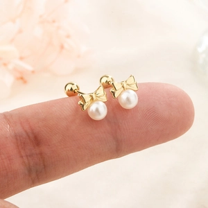 Boucles d'oreilles nœud doré avec perles blanches et fermoir à vis sur le doigt