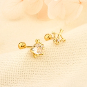 Detail view of gold cupid arrow and heart zircon screw back earrings on beige fabric