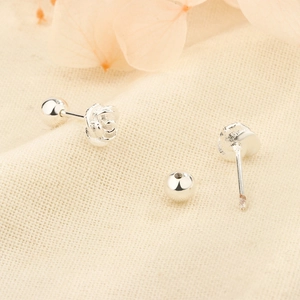 Elegant silver rose stud earrings with secure screw back closure on beige fabric