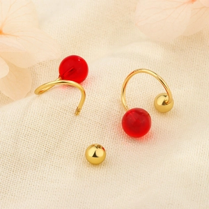 Détail de boucles d'oreilles S925 dorées avec perles rouges et fermoir à vis sur tissu